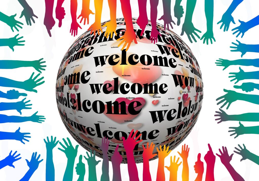 Viele Bunte Hände Zeigen auf eine Kugel, auf der in verschiedenen Sprachen das Wort "Willkommen" steht
